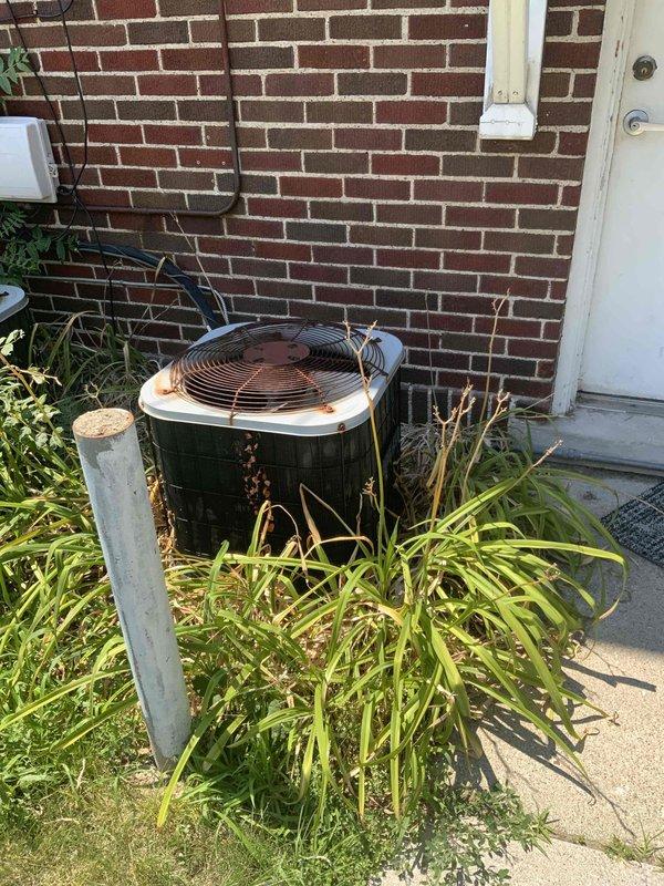 Completed HVAC system evaluation for residential replacement estimate at return customer's different apartment unit. Assessed aging outdoor condenser unit positioned against brick exterior, noting weathered condition with visible dirt accumulation and overgrown vegetation obstructing proper airflow around base of equipment. Documented existing electrical service configuration including meter location, panel access, and conduit routing for replacement planning purposes. Photographed current equipment placement, clearance requirements, and utility connections to provide comprehensive assessment for full system replacement proposal.