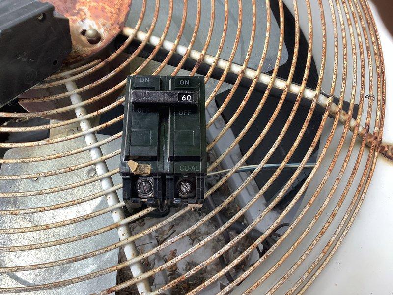 Responded to report of AC breaker tripping repeatedly over a two-day period. Upon inspection, found outdoor condensing unit with 60-amp CU-AL rated circuit breaker and electrical components showing significant weathering, corrosion, and oxidation. Documented condition of contactor, disconnect switch, and wire terminals at top of unit. Extensive rust present on metal fan guard and housing surfaces indicated prolonged environmental exposure. Photographed electrical connections and breaker assembly for service records.