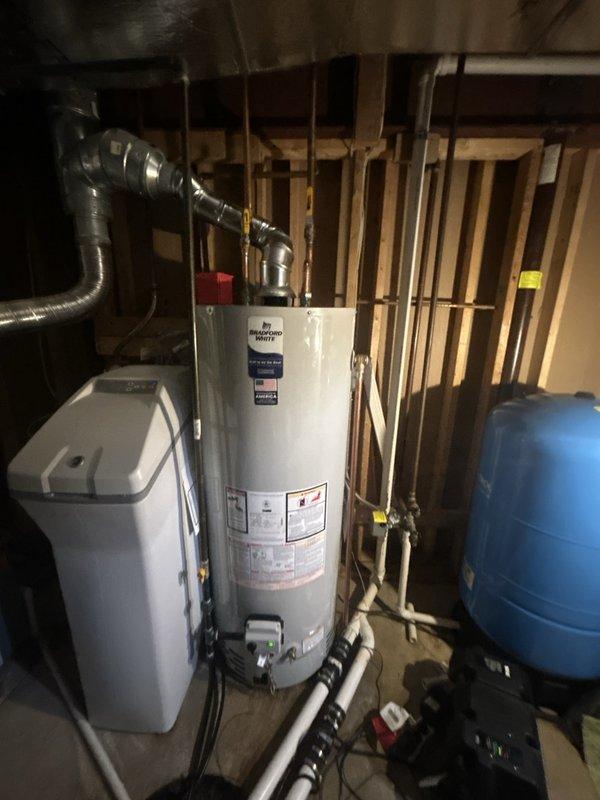 Successfully installed a Bradford White 50-gallon tanked water heater (model RG250S6N) in the basement utility area. Completed all copper piping connections at the top of the unit, installed proper shut-off valves, and connected white PVC drainage lines at the base with appropriate securing straps. Integrated the new water heater with the existing plumbing system, including coordination with the adjacent water treatment system and pressure tank. All connections were tested for proper operation and leak-free performance.