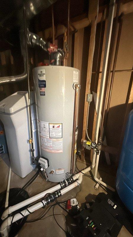 Successfully installed a Bradford White 50-gallon tanked water heater (model RG250S6N) in the basement utility area. Completed all copper piping connections at the top of the unit, installed proper shut-off valves, and connected white PVC drainage lines at the base with appropriate securing straps. Integrated the new water heater with the existing plumbing system, including coordination with the adjacent water treatment system and pressure tank. All connections were tested for proper operation and leak-free performance.
