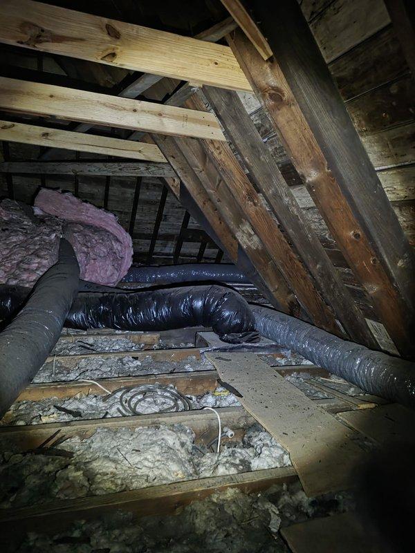 Conducted comprehensive attic inspection to assess existing air conditioning system and provide replacement estimate. Evaluated attic-mounted HVAC equipment, existing ductwork configuration, structural access points, and insulation conditions. Documented current system layout including flexible duct routing, PVC condensate drainage, ventilation pathways, and available clearances for equipment replacement. Photographed attic space showing wooden framing, existing black flexible ductwork, insulation materials, and brick chimney structure to support replacement recommendations and equipment sizing calculations.