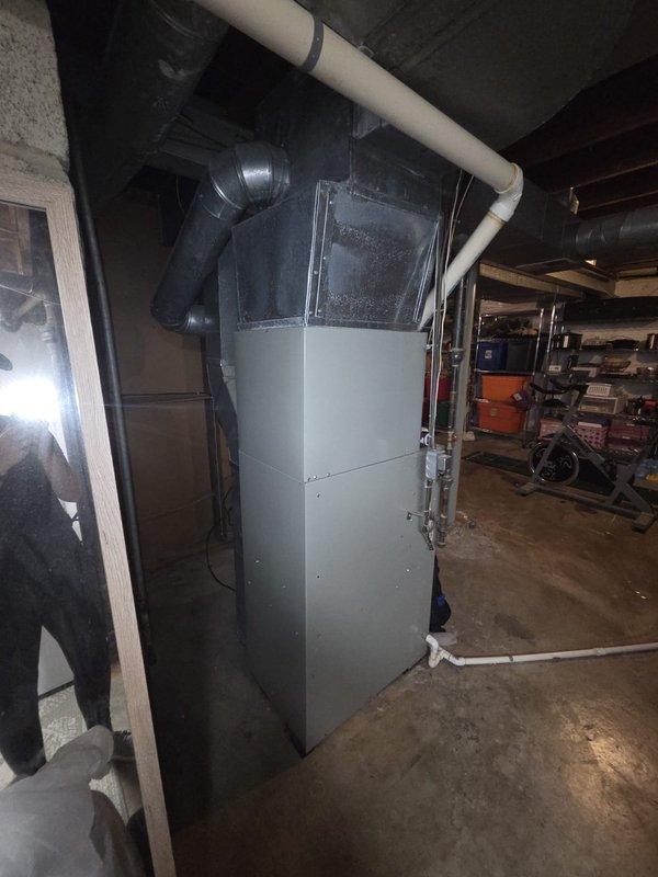 Conducted comprehensive assessment of existing HVAC system for complete replacement estimate. Evaluated gas furnace and air conditioning equipment located in basement installation. Documented current forced-air heating unit with gray metal casing, associated ductwork configuration, and PVC condensate drainage system. Inspected existing thermostat control wiring and terminal connections to determine compatibility requirements for new equipment installation. Photographed equipment specifications, spatial constraints, and existing infrastructure to develop accurate replacement proposal for complete heating and cooling system upgrade.