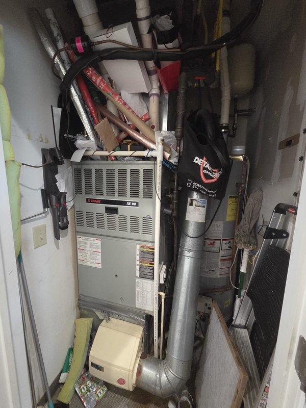 Completed estimate for complete HVAC system replacement in residential utility closet with cramped working conditions. Assessed existing Trane furnace system with 100,000 BTU input capacity, current air filtration at 20x20x1 specification, and 2-3 inch PVC venting configuration. Documented existing equipment layout including furnace unit, air conditioning condenser, water heater, and associated ductwork in confined mechanical room with limited accessibility. Evaluated current installation featuring beige furnace with white louvered panel, silver metallic supply ductwork, gray PVC condensate piping with insulation tape, black flexible ducting, and copper refrigerant lines. Recommended humidifier replacement as part of system upgrade. Recorded technical specifications for replacement system including BTU ratings, air filter dimensions, condenser specifications, refrigerant piping requirements, electrical specifications, and thermostat placement. Photographed existing equipment arrangemen