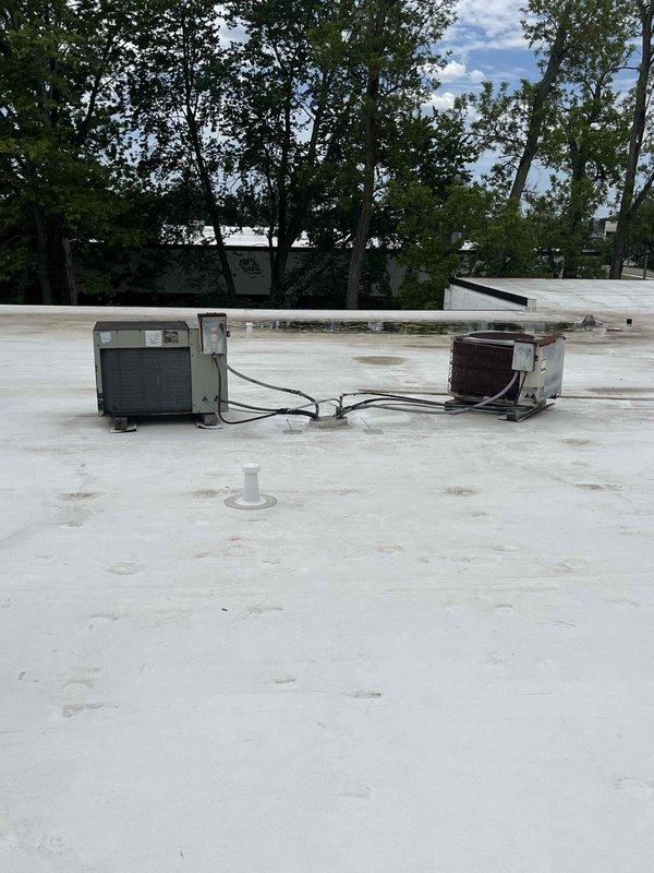Responded to commercial service call for two non-operational rooftop units (RTUs) on flat membrane roof. Upon arrival, accessed roof and inspected both units - one light gray/beige condenser showing moderate wear and one significantly aged unit with brown weathered casing exhibiting extensive rust and deterioration. Evaluated refrigerant line sets, electrical conduit connections, and overall system condition. Documented existing rooftop infrastructure including cable routing, insulated line sets, roof penetrations, and membrane patches indicating previous repair work. Both units assessed as beyond economical repair due to age, corrosion, and component failure. Provided comprehensive replacement estimate for both RTU systems including removal of existing equipment, proper disposal, new unit installation with updated refrigerant lines, electrical connections, roof curb adapters, and membrane sealing to maintain roof integrity.