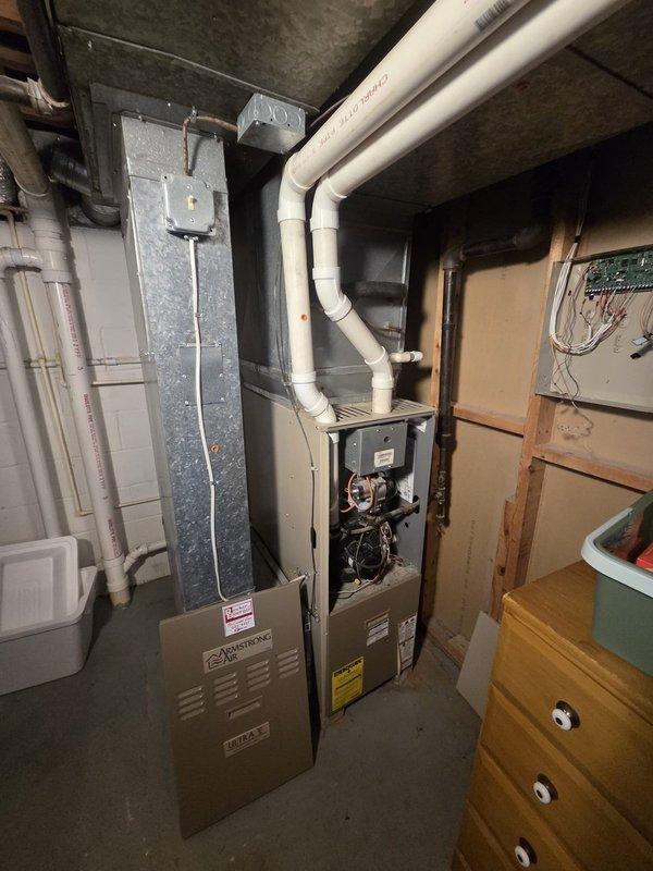Conducted comprehensive evaluation of existing 1994 Goodman HVAC system utilizing R22 refrigerant for complete replacement estimate. Inspected basement-installed furnace unit with exposed cabinet access panel, documenting internal mechanical components, wiring configuration, and overall equipment condition. Assessed white PVC venting system routing from furnace through ceiling, dark gray metal supply plenum, and existing ductwork infrastructure. Evaluated thermostat wiring interface showing standard color-coded connections including Y (compressor), G (fan), W (heat), C (common), R (power), and OB (reversing valve) terminals. Photographed all equipment, connections, and installation layout to prepare detailed replacement proposal for both furnace and air conditioning components.