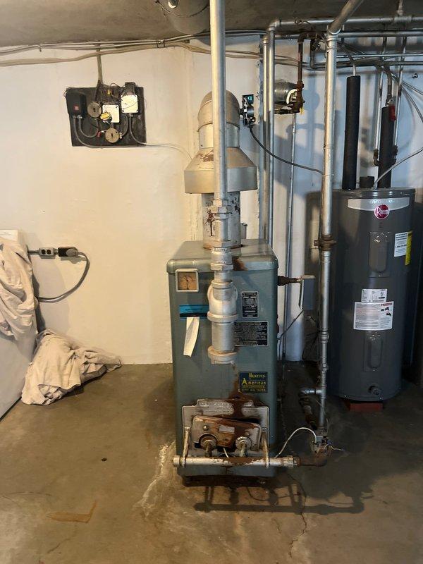 Conducted on-site evaluation of existing residential boiler system and domestic hot water heater in basement mechanical room. Assessed teal-colored boiler unit with base-mounted circulator pump assembly and adjacent Rheem water heater for replacement consideration. Documented current equipment configuration, piping connections, electrical controls, and fire suppression system components including dual red circulation pumps. Photographed existing installation conditions to provide comprehensive estimate for boiler replacement and system upgrades.