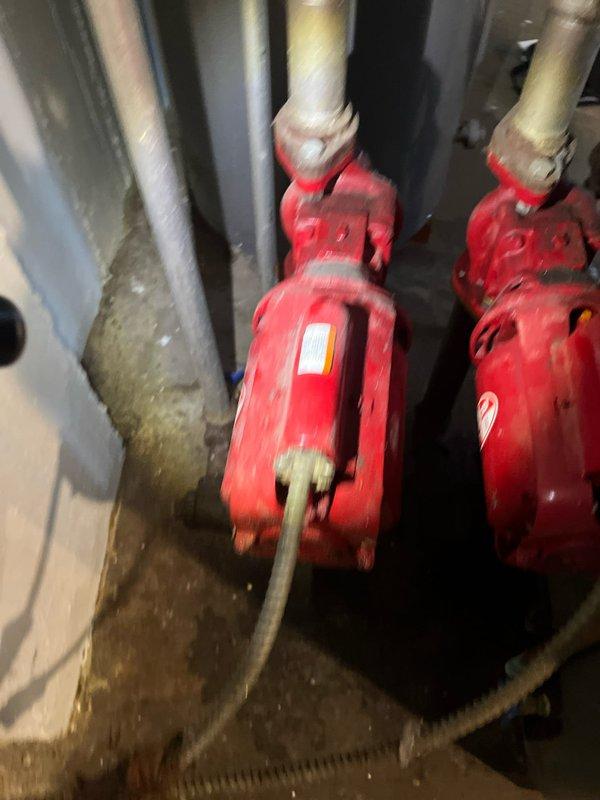 Conducted on-site evaluation of existing residential boiler system and domestic hot water heater in basement mechanical room. Assessed teal-colored boiler unit with base-mounted circulator pump assembly and adjacent Rheem water heater for replacement consideration. Documented current equipment configuration, piping connections, electrical controls, and fire suppression system components including dual red circulation pumps. Photographed existing installation conditions to provide comprehensive estimate for boiler replacement and system upgrades.