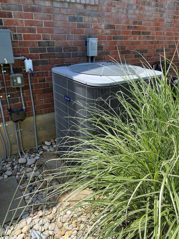 Conducted comprehensive site evaluation for complete HVAC system replacement at residential property. Assessed existing outdoor condenser unit positioned against brick exterior wall, documenting current equipment configuration including electrical disconnect boxes, conduit routing, and mounting location. Photographed equipment placement in relation to landscaping features, concrete pad condition, and clearance requirements for proper airflow and serviceability. Evaluated accessibility for removal of existing unit and installation of replacement equipment, noting ornamental grass plantings and river rock landscaping that may require temporary relocation during changeout. Documented electrical service components mounted on exterior wall to determine compatibility with proposed replacement system. Prepared detailed estimate for full system replacement including equipment specifications, installation requirements, and necessary modifications to existing infrastructure.