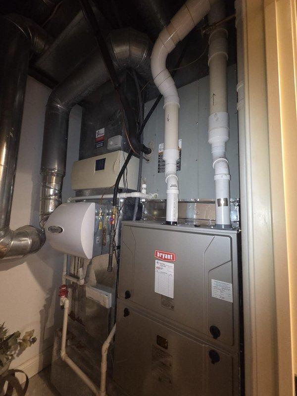 Conducted comprehensive assessment of existing residential HVAC system for replacement of two air conditioning units. Evaluated current Bryant furnace installation, associated ductwork configuration, and integrated humidification system in mechanical room. Documented existing equipment specifications, condensate drainage lines, PVC venting systems, and electrical connections. Inspected flexible and rigid ductwork routing, air handler components, and system controls to determine compatibility requirements for new AC unit installations. Photographed current setup including furnace positioning, plumbing connections, and available workspace for equipment replacement planning.