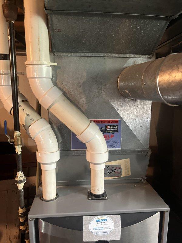 Completed estimate for air conditioning system replacement at residential property. Evaluated existing HVAC system installation in basement utility area, including gray metal furnace/air handler unit with white PVC condensate drain lines configured in S-shape with multiple elbow joints. Assessed copper gas line with brass shutoff valve, brown metal ductwork for air distribution network, and white PVC plumbing infrastructure with blue-handled ball valve for water flow control. Documented current system configuration and components to provide replacement options and recommendations for new AC equipment installation.
