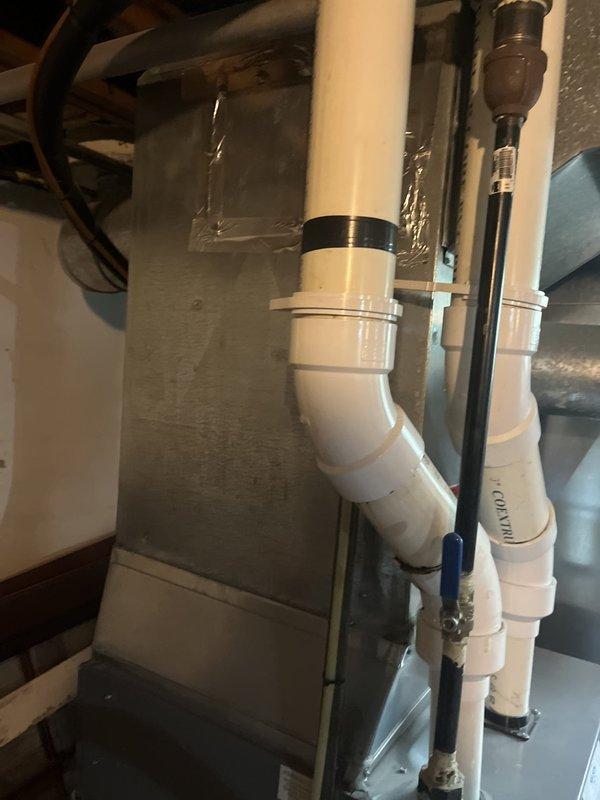 Completed estimate for air conditioning system replacement at residential property. Evaluated existing HVAC system installation in basement utility area, including gray metal furnace/air handler unit with white PVC condensate drain lines configured in S-shape with multiple elbow joints. Assessed copper gas line with brass shutoff valve, brown metal ductwork for air distribution network, and white PVC plumbing infrastructure with blue-handled ball valve for water flow control. Documented current system configuration and components to provide replacement options and recommendations for new AC equipment installation.