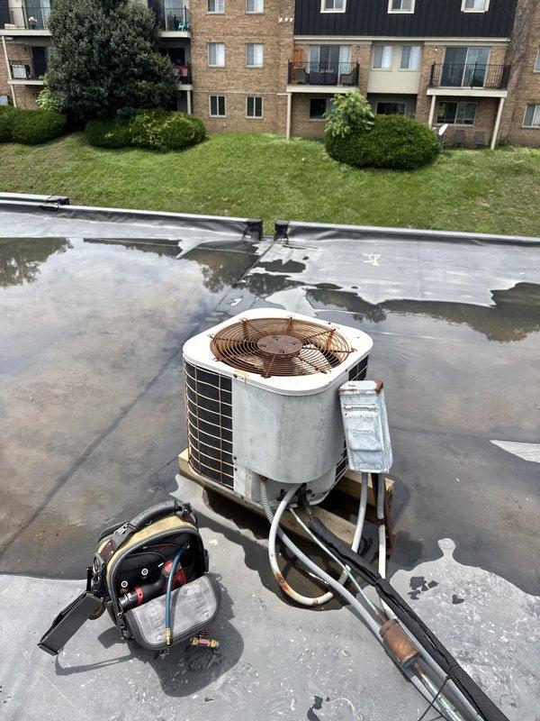 Responded to service call for commercial rooftop A/C unit not cooling at vacant property. Upon arrival, performed diagnostic evaluation of packaged rooftop unit showing signs of weathering and age. Inspected condenser unit exterior panels, coil condition, and refrigerant line set with insulation. Checked electrical disconnect and verified power supply to unit. Assessed standing water on roof membrane surrounding equipment, noting potential drainage concerns. Documented unit condition including weathered housing, discolored exterior panels, and exposed condenser coil fins. Unit required further diagnostics to determine root cause of cooling deficiency in refrigerant lines.