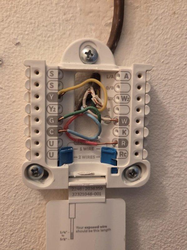 Performed comprehensive HVAC system assessment for air conditioning replacement estimate. Documented existing thermostat wiring configuration showing standard color-coded connections (yellow, green, red, and blue wires) at terminal block, and photographed current basement mechanical equipment including furnace unit with overhead ductwork and water heater to determine replacement specifications and installation requirements.