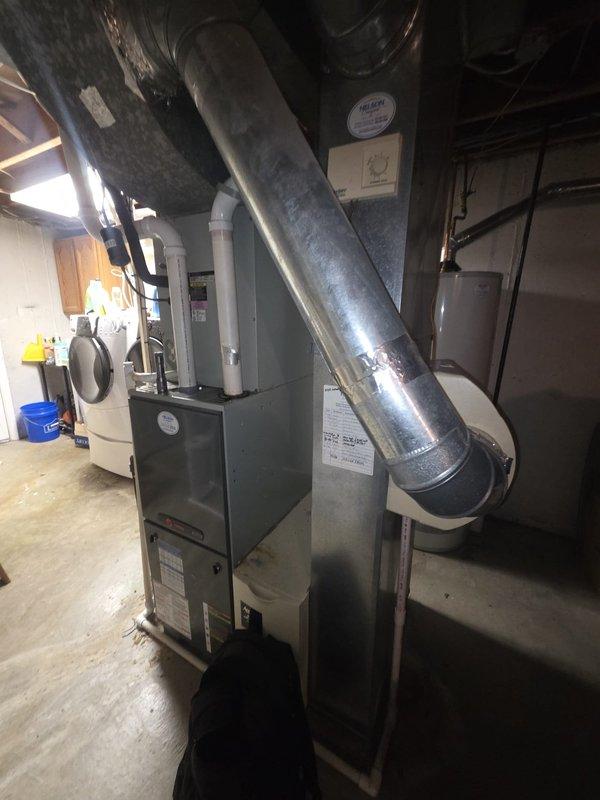 Performed comprehensive HVAC system assessment for air conditioning replacement estimate. Documented existing thermostat wiring configuration showing standard color-coded connections (yellow, green, red, and blue wires) at terminal block, and photographed current basement mechanical equipment including furnace unit with overhead ductwork and water heater to determine replacement specifications and installation requirements.