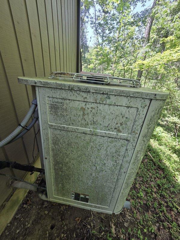 Conducted comprehensive site assessment for geothermal system installation at residential property. Existing outdoor heat pump unit exhibits severe environmental deterioration with extensive mold, mildew, and organic growth on metal casing, indicating end of service life and need for replacement. Documented damaged exterior refrigerant line insulation with torn jacketing and exposed degraded material requiring immediate replacement. Evaluated electrical components, conduit routing, and wall penetrations for geothermal system integration. Photographed existing equipment condition and installation area to develop accurate proposal for geothermal heat pump system replacement.