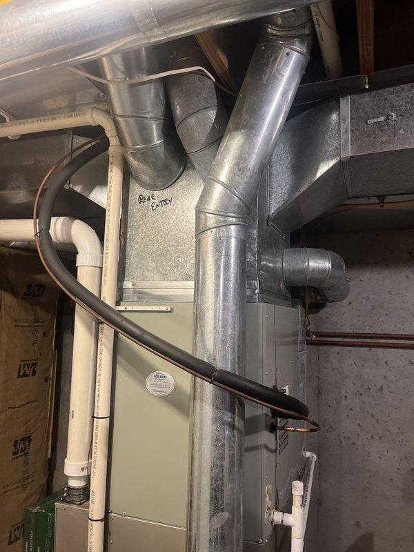 Conducted comprehensive HVAC system assessment for complete furnace and air handler replacement in residential basement utility space. Documented existing beige-colored furnace unit with associated galvanized sheet metal ductwork, flexible duct connections, PVC condensate drainage lines, and copper refrigerant piping. Photographed current system configuration including vertical and horizontal duct runs, exposed pink fiberglass insulation in wall cavities, and concrete block wall mounting location. Evaluated existing ENERGYSOURCE labeled unit for replacement specifications and measured clearances for new equipment installation. Provided detailed estimate for complete system replacement including removal of existing furnace, installation of new high-efficiency unit, ductwork modifications as needed, and proper connection of all utilities and drainage systems.