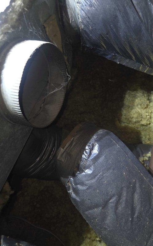 Conducted comprehensive estimate for ductwork replacement in attic space. Inspected existing galvanized sheet metal Y-junction plenum connecting to flexible ductwork, noting dust accumulation and age-related wear on metal surfaces. Evaluated black flexible ducting with insulation showing deteriorated tape seals and assessed routing through confined crawl space areas with fiberglass insulation present. Documented current duct configuration including rigid circular transition fittings and rectangular plenum with visible seams for replacement specifications.