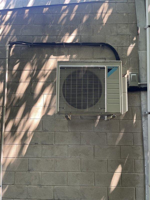 Conducted commercial estimate for complete mini-split system replacement. Existing Daikin outdoor condenser unit mounted on exterior concrete block wall was evaluated and determined to be non-operational. Documented current installation including wall-mounted condensing unit with protective overhead cover, refrigerant line connections, electrical disconnect box, and associated conduit routing for replacement specifications.