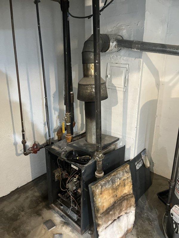 Conducted comprehensive assessment of residential boiler heating system showing visible signs of deterioration. Documented extensive corrosion, water damage, and mineral deposits on lower front panel of boiler unit, indicating potential leak or condensation issues requiring attention. Evaluated existing piping configuration including copper supply lines, gate valves, and connection points throughout the system. Photographed current condition of equipment and plumbing assembly for estimate preparation and recommended replacement or repair options based on observed wear patterns and system age.