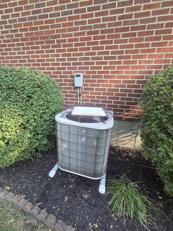 Conducted comprehensive estimate for complete HVAC system replacement including furnace and air conditioning equipment. Evaluated existing outdoor condenser unit positioned on gravel pad against exterior brick wall, noting current copper refrigerant line configuration and electrical disconnect setup. Assessed interior analog thermostat system with exposed mechanical components requiring modernization. Documented equipment specifications and site conditions through photographic records. Presented replacement options for gas furnace and air conditioning system with available promotional pricing for bundled installation.