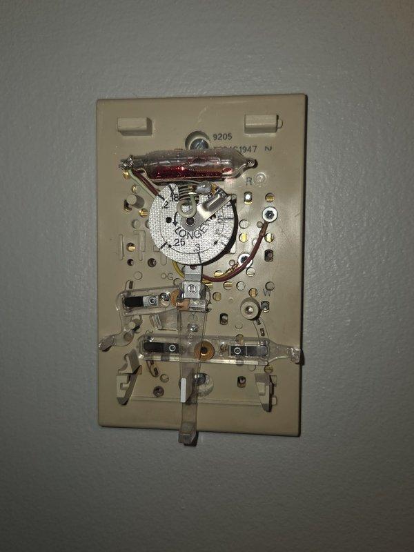 Conducted comprehensive estimate for complete HVAC system replacement including furnace and air conditioning equipment. Evaluated existing outdoor condenser unit positioned on gravel pad against exterior brick wall, noting current copper refrigerant line configuration and electrical disconnect setup. Assessed interior analog thermostat system with exposed mechanical components requiring modernization. Documented equipment specifications and site conditions through photographic records. Presented replacement options for gas furnace and air conditioning system with available promotional pricing for bundled installation.