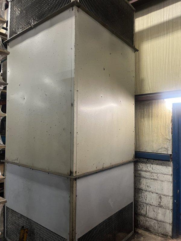 Conducted on-site estimate for commercial furnace replacement at industrial facility. Unit is a ground-mounted packaged heating system serving the factory area, showing significant age and wear with visible dirt accumulation, surface staining, and weathering on exterior metal panels. Assessed existing beige metal cabinet-style unit with ventilation grilles, galvanized ductwork connection, blower assembly, and electrical control panel protected by safety barriers. Documented equipment condition through photographs and evaluated replacement requirements for continued operation of facility heating system.
