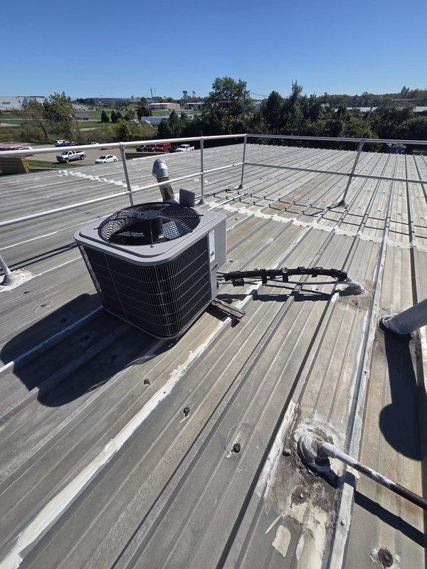 Conducted comprehensive site assessment for commercial rooftop unit replacement at office facility. Evaluated existing RTU positioned on corrugated metal roof with safety railing system, documenting unit condition, mounting configuration, and accessibility for replacement. Inspected interior mechanical space and air handler equipment, noting existing ductwork connections including flexible ducting and PVC condensate drainage lines with compression fittings. Photographed rooftop installation showing cylindrical condenser unit on white platform base with vertical PVC vent pipe, as well as basement mechanical room revealing HVAC equipment with exposed wooden beam ceiling structure and visible water staining. Assessed structural considerations for new unit installation including roof penetrations, electrical service routing, and existing piping infrastructure. Provided technical recommendations for equipment replacement including proper sizing requirements, mounting specifications, and con