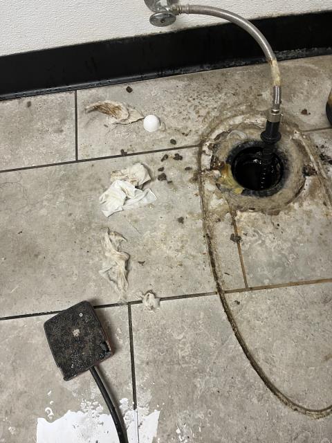 Arrived to find the sewer line clogged and coming up from under the roof molted toilet and into the mop sink in the janitors closet. 
  Pulled the toilet and ran a mainline snake with a bare cable down the toilet flange. 
  Got the line to flow about 125 feet into the flange. 
  Ran water into the mop sink, the bathroom sink, and down the toilet flange to test. The sewer line is draining at this time. 
  Pulled back thick toilet paper and some wipes on the cable. 
  Reset the toilet with a new 3” wax ring. 
  Flushed the toilet to test. It’s flushing at this time. 