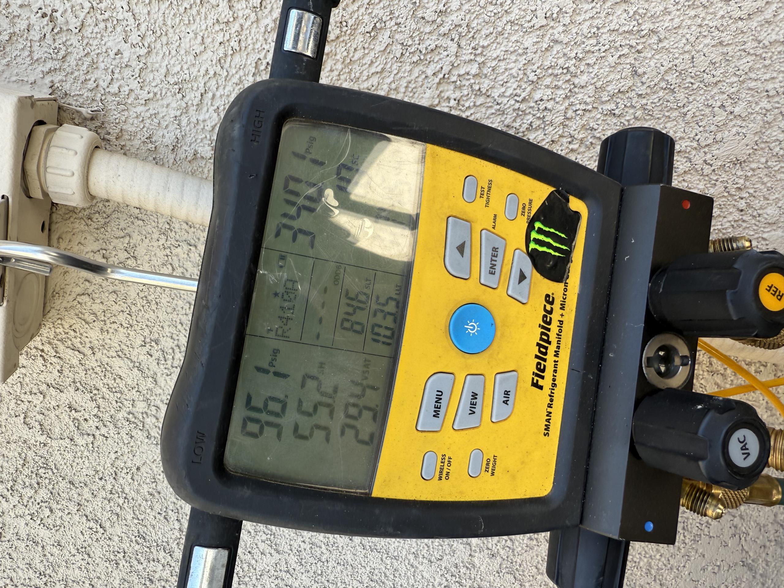 The technician arrived at the customer's house to investigate a cooling issue. The customer reported that the rear end of the house did not receive adequate cooling during a party. The technician activated both systems to examine them. The front unit was found to be adequately charged, but the capacitor showed signs of pitting, leading to a recommendation for its replacement. The condenser fan motor was covered in oil, but there was no play in the shaft. The technician advised replacing the motor due to the loss of lubricant, which could result in overheating and seizing, potentially causing irreversible damage to the compressor and increasing repair costs. The technician verified that the capacitor was within factory specifications and all refrigerant levels were within the acceptable range. The technician then proceeded to the rear unit at the back of the house, where gauges were connected and it was discovered that the system was significantly low on Freon. Power was shut down to ch