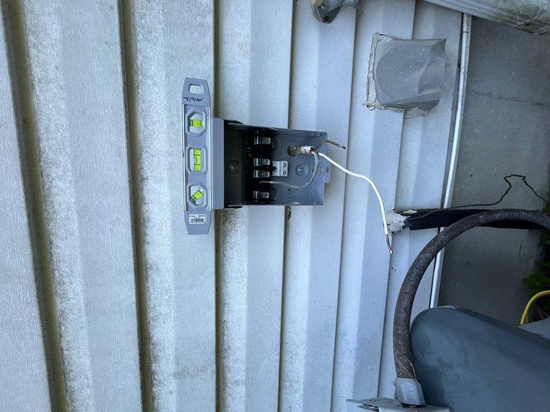 Completed installation of air conditioning condenser unit on exterior of building with corrugated metal siding. Mounted electrical disconnect box to wall, ran white electrical conduit with proper wiring connections, and verified level alignment during installation. Installed flexible ductwork penetration through building wall to connect condenser unit, positioned unit on ground-level pad, and completed all electrical terminations at disconnect. System installed per manufacturer specifications and ready for operation.