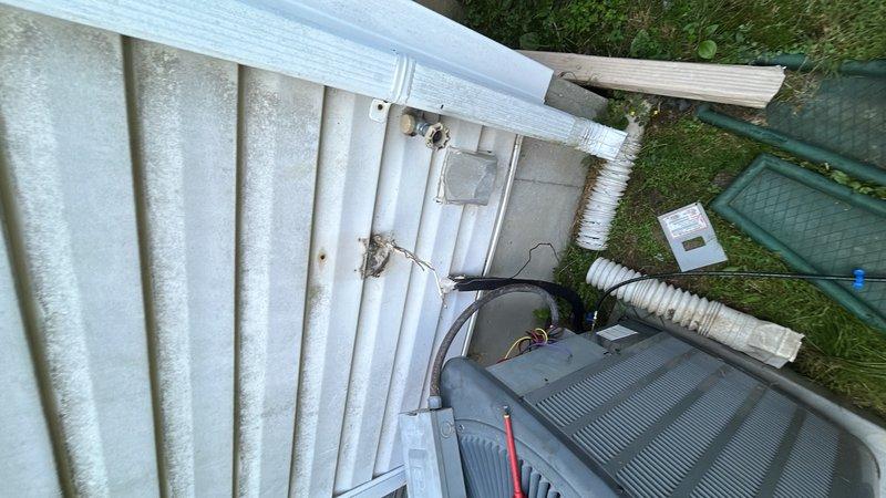 Completed installation of air conditioning condenser unit on exterior of building with corrugated metal siding. Mounted electrical disconnect box to wall, ran white electrical conduit with proper wiring connections, and verified level alignment during installation. Installed flexible ductwork penetration through building wall to connect condenser unit, positioned unit on ground-level pad, and completed all electrical terminations at disconnect. System installed per manufacturer specifications and ready for operation.
