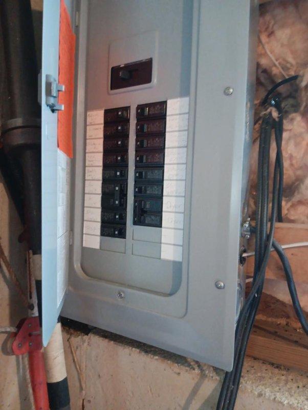Completed installation of gas line and electrical panel in residential construction area. Installed black metal gas pipe with brass connector and flexible braided high-pressure line for appliance connection, routed yellow flexible conduit through wooden framing, and mounted electrical panel box with circuit breakers on exposed wall studs with proper wire management through insulated cavity.