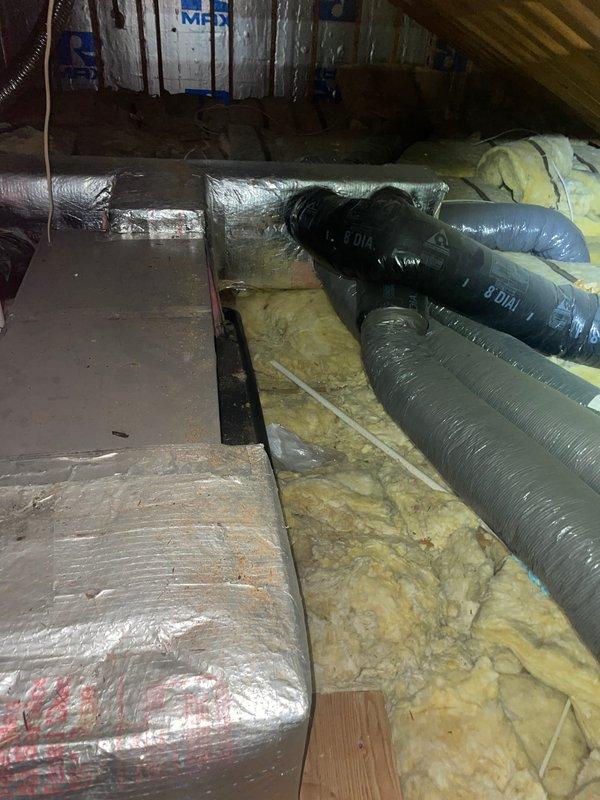 Completed comfort call inspection of residential HVAC system located in attic space. Documented existing air handler unit with associated ductwork, refrigerant lines, and electrical connections. All components appeared to be functioning within normal parameters, with reflective insulated ductwork properly installed and fiberglass insulation present between floor joists throughout the attic space.
