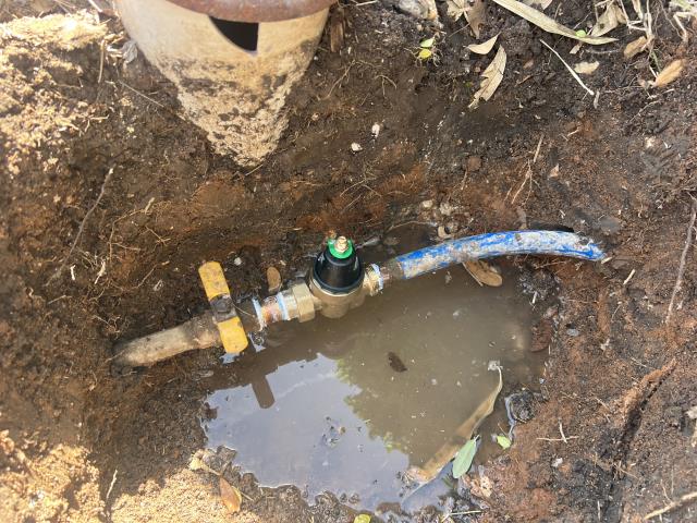 Supply and install new pressure reducing valve and 2 gallon expansion tank to match new water pressure. Water supply line installation with pressure reducing valve and blue piping in a trench, surrounded by dirt and water, illustrating plumbing work by American Eagle Plumbing in Pflugerville, TX.