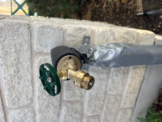 Supply and install new outdoor spigot with a code approved vacuum breaker. Remove ans dispose of the old spigot. Newly installed outdoor spigot with green handle and brass fittings, featuring a vacuum breaker, mounted on a stone wall, showcasing plumbing upgrade in Pflugerville, TX.