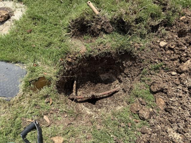 Excavated area revealing a buried pipe, surrounded by disturbed soil and grass, related to plumbing services in Leander, TX.