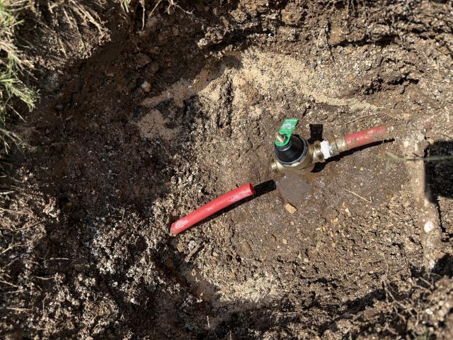 Pressure reducing valve installation in a dug-out trench with red piping, related to plumbing services in Leander, TX.