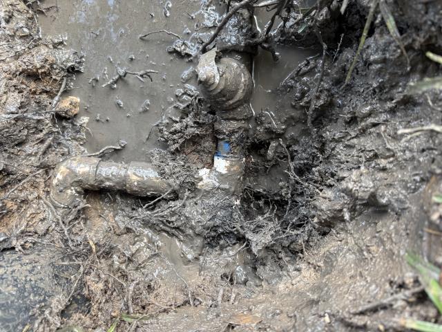 Exposed plumbing pipes covered in mud and debris, indicating potential issues with water flow or leaks in a residential setting.