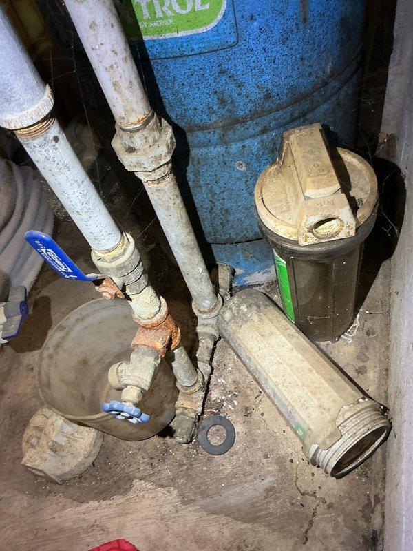 Performed scheduled preventative maintenance on water pressure tank system in basement. Upon inspection, found significant corrosion and mineral buildup on connecting pipes and joints, particularly at connection points. Serviced aging water treatment system, addressing the leaking water storage tank (approximately 20 gallon) which showed considerable discoloration and grime accumulation on the lower section.
