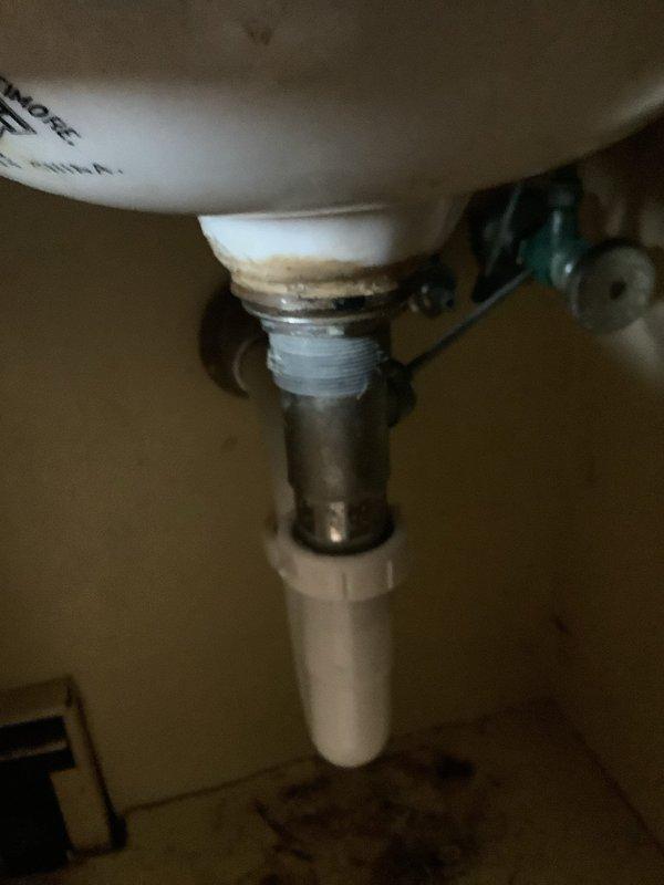 Replaced existing two-handle bathroom faucet with new single-handle chrome model, addressing leak at the pipe connection beneath lavatory sink. Observed significant mineral deposits and corrosion at the threaded drain connection, which was contributing to the leak issue.