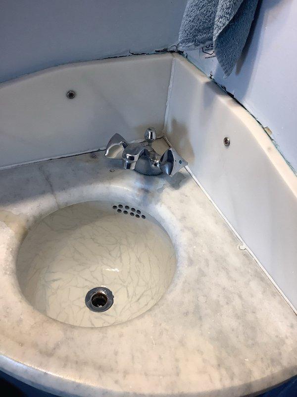 Replaced existing two-handle bathroom faucet with new single-handle chrome model, addressing leak at the pipe connection beneath lavatory sink. Observed significant mineral deposits and corrosion at the threaded drain connection, which was contributing to the leak issue.