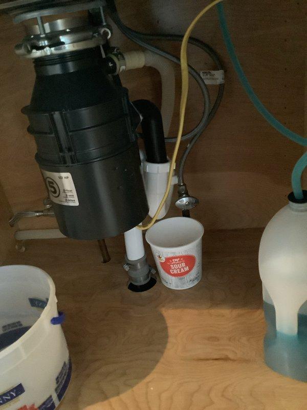 Responded to emergency call for active leak under kitchen sink. Upon arrival, found water leaking from disposal or drain connections, with customer using bucket for temporary containment. Inspected garbage disposal unit and associated drain plumbing, identified source of leak, and performed necessary repairs to stop water flow and restore proper drainage function.