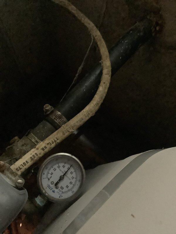 Responded to service call for active drip/leak at temperature and pressure relief valve on well pressure tank system. Upon inspection, confirmed leak at T&P relief valve near well tank installed in 2018. Photographed existing conditions showing turquoise pressure tank, white expansion tank, copper piping with shut-off valves, and pressure gauge assembly. Placed collection bucket beneath leak to prevent water damage. Assessed system components and documented leak source for repair recommendation.
