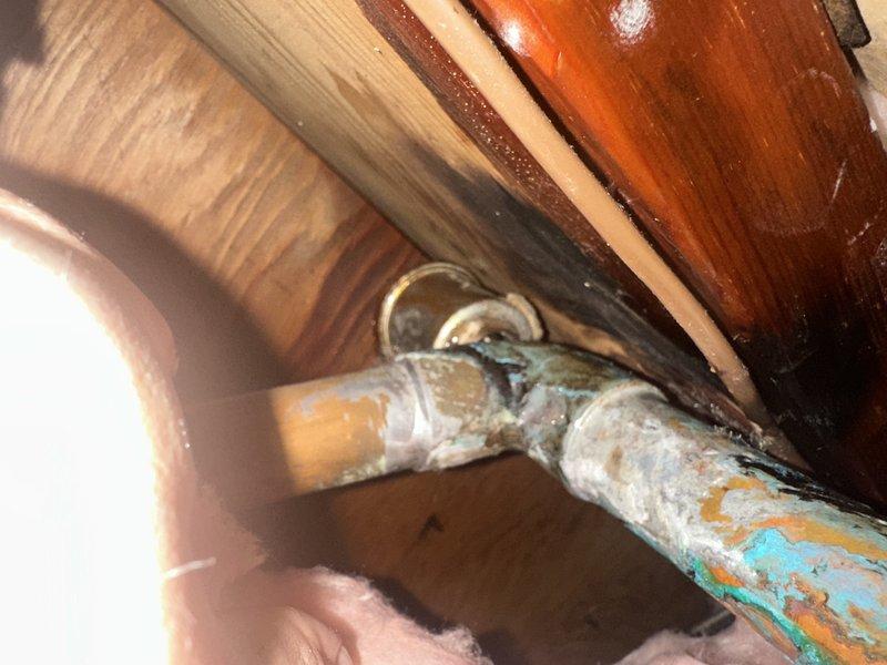 Responded to leak complaint above water heater at commercial location. Upon inspection, identified failed automatic air vent on water heater system as source of leak. Air vent showed signs of corrosion and deterioration on copper piping connections. Accessed confined crawl space area to assess piping condition and extent of water damage. Observed heavy oxidation and patina buildup on copper pipe fittings and joints, indicating prolonged moisture exposure. Documented corroded connections and deteriorated automatic air vent assembly with photographs for service records. Confirmed leak source and provided assessment of required repairs to restore proper water heater operation.