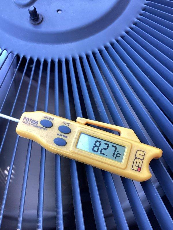 Completed comprehensive air conditioning tune-up and maintenance on residential HVAC system originally installed in August 2018. Performed diagnostic temperature measurements on condenser unit, recording ambient temperature readings of 82.7°F at the heat exchanger assembly. Inspected radial fin condenser coil and verified proper airflow through the unit, with all fins intact and properly aligned for optimal heat transfer efficiency.