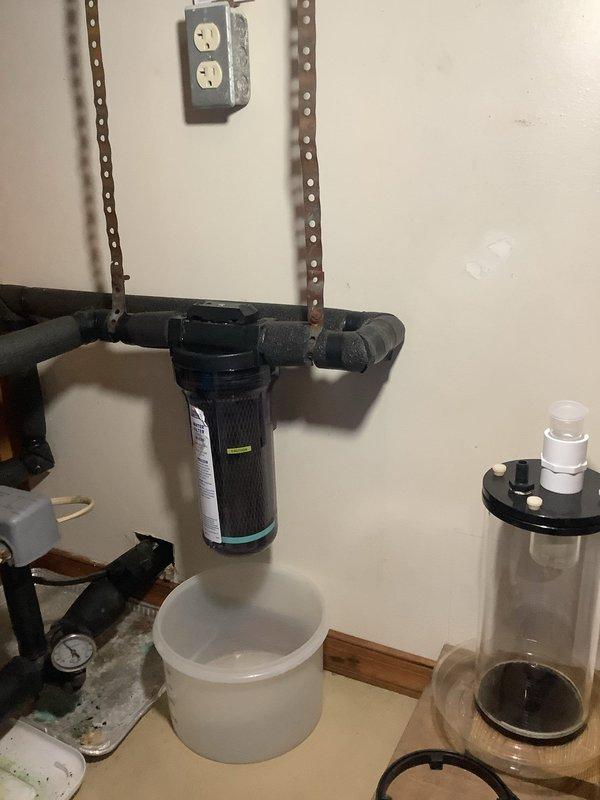 Responded to troubleshoot ongoing water system issues including recurring low water pressure, filter contamination with black sediment, and persistent leaking at the whole house water filter assembly. Conducted comprehensive inspection of the complete water system from well to point-of-entry equipment, examining all plumbing connections, pressure regulation components, and filtration hardware. Documented existing conditions with photographs showing the insulated pipe network, pressure gauge, filter housing with visible leak collection pans positioned beneath the assembly, and associated water treatment components. Identified the whole house filter as the primary source of leaking, which had progressed from an initial leak that temporarily stopped after filter replacement to a current slow drip condition. Noted significant black sediment accumulation requiring multiple filter changes within a short timeframe, indicating potential issues with well water quality or system contamination. E