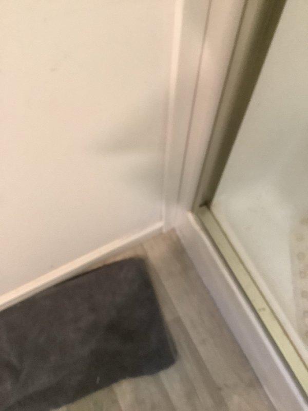 Responded to dispatch for bathroom leak investigation at walk-in shower area. Upon arrival, confirmed active water intrusion occurring after shower use, with visible moisture emerging from beneath tub and saturating floor covering. Conducted thorough inspection of shower pan, drain assembly, and surrounding plumbing connections to identify source of leak. Documented conditions with photographs showing water damage to flooring, baseboards, and wall-to-floor junctions in affected bathroom area for further diagnostic evaluation and repair planning.