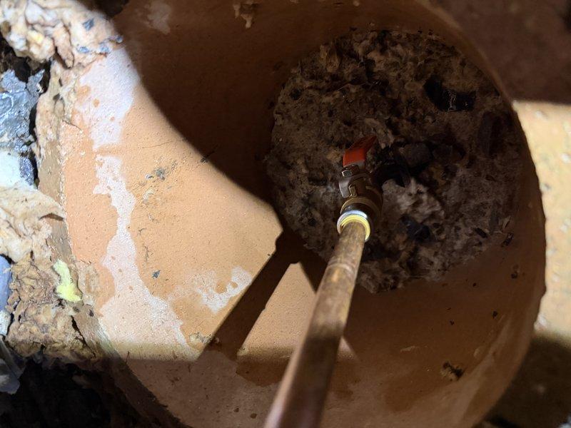 Responded to after-hours emergency call for leaking pipe in crawl space. Upon arrival, accessed utility area and performed electrical testing on wiring near affected plumbing components to ensure safe working conditions. Located source of leak at underground pipe connection point with significant water accumulation and sediment buildup in access pit. Inspected shutoff valve assembly with red handle mechanism and surrounding copper piping. Documented deteriorated conditions including compromised insulation, moisture damage, and debris accumulation throughout work area. Provided photographic documentation of electrical testing procedures and valve access point conditions for estimate preparation and repair planning.