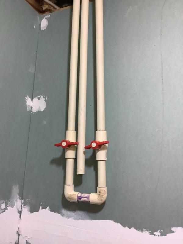 Installed Water Max WT water treatment system with acid neutralizer and iron-removing capabilities to address low pH water (5.8) and fine iron-rich sediment causing rust-colored residue buildup in plumbing fixtures and CPVC piping. System includes gray cylindrical softener tank (model WM 20MXQ 8IG) with integrated filtration components connected via PVC and blue CPVC piping with red ball valve shutoffs for system isolation. Installation required wall penetrations and plumbing modifications to integrate treatment system into existing water supply line, with patching and finishing work performed on interior wall surfaces around new piping runs.