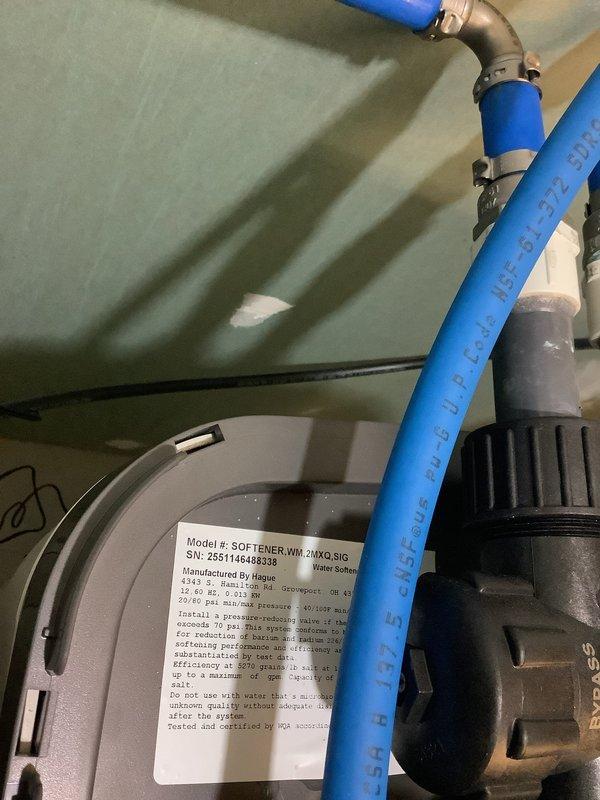 Installed Water Max WT water treatment system with acid neutralizer and iron-removing capabilities to address low pH water (5.8) and fine iron-rich sediment causing rust-colored residue buildup in plumbing fixtures and CPVC piping. System includes gray cylindrical softener tank (model WM 20MXQ 8IG) with integrated filtration components connected via PVC and blue CPVC piping with red ball valve shutoffs for system isolation. Installation required wall penetrations and plumbing modifications to integrate treatment system into existing water supply line, with patching and finishing work performed on interior wall surfaces around new piping runs.